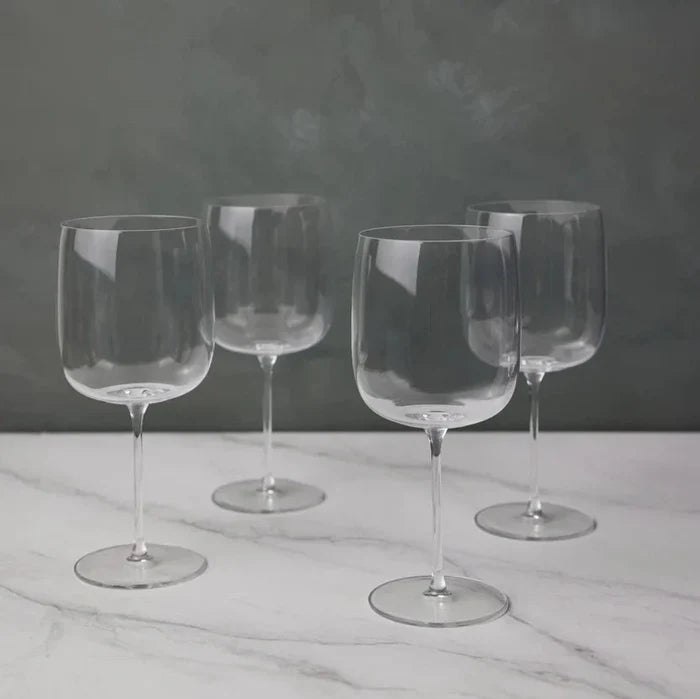 Four empty, clear Borough Barware glasses by LSA are arranged on a white marble surface with a gray textured background. Their reflections add elegance, making this Set of 4 a stylish addition to any barware collection.