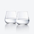 Two Chateau Barware glasses by Baccarat, half-filled with water, stand side by side on a reflective white surface with a light gray background.